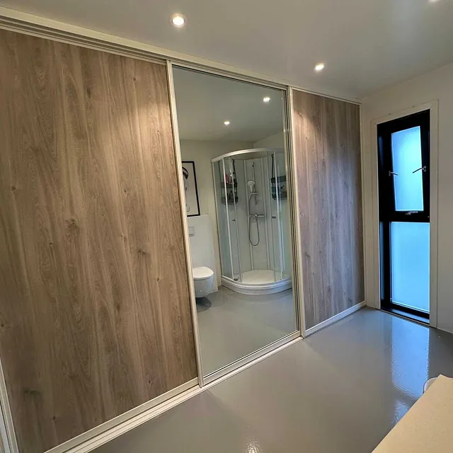 Moderne baderom med dusjkabinett, tredekor på vegger og speilskyvedør.